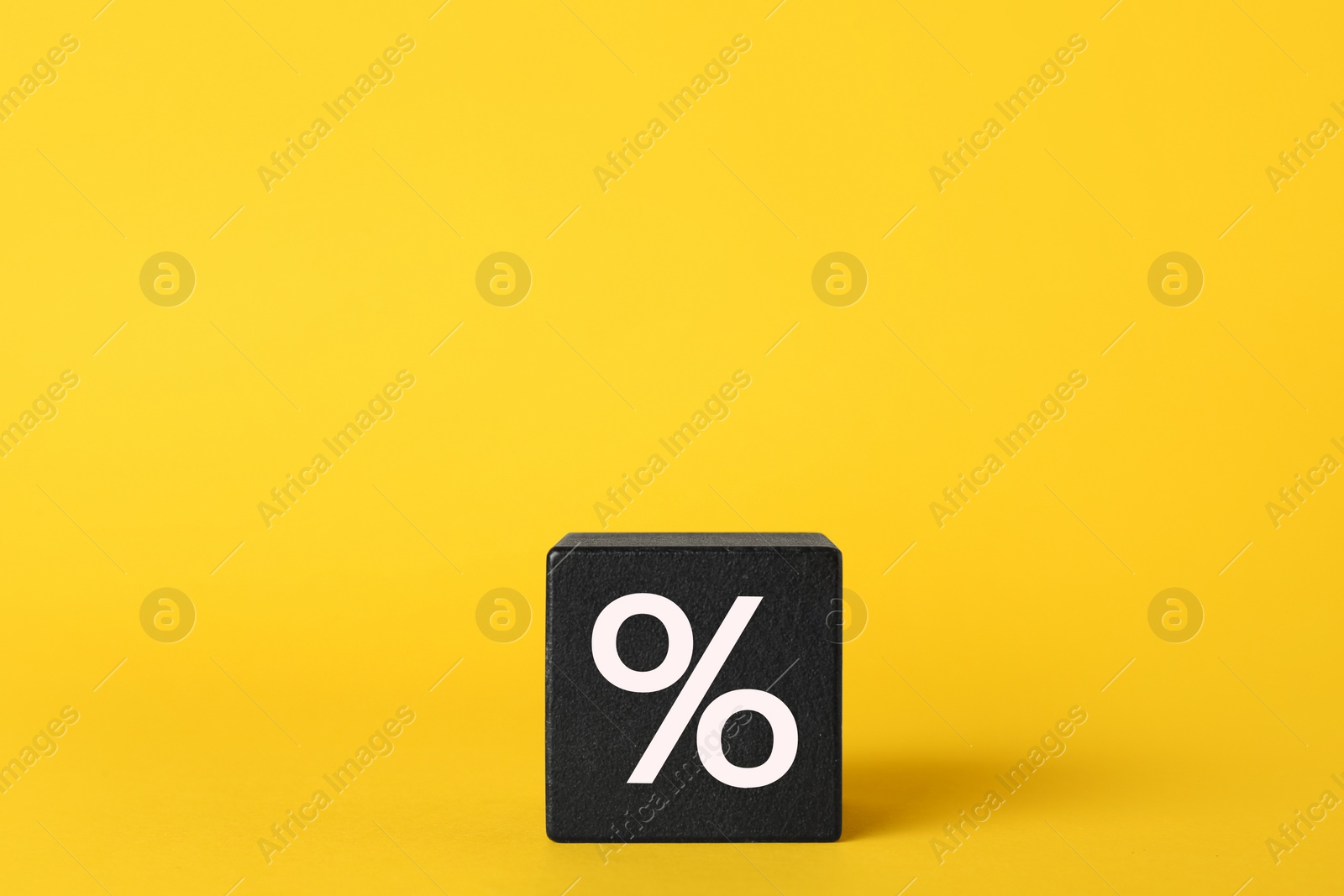 Photo of Black cube with percent sign on yellow background. Space for text