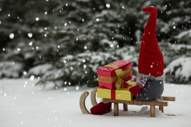 Wooden sleigh with Christmas gnome and gift boxes on snow outdoors. Space for text