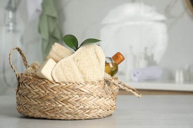 Photo of Natural loofah sponges and soap bar in wicker basket on table indoors
