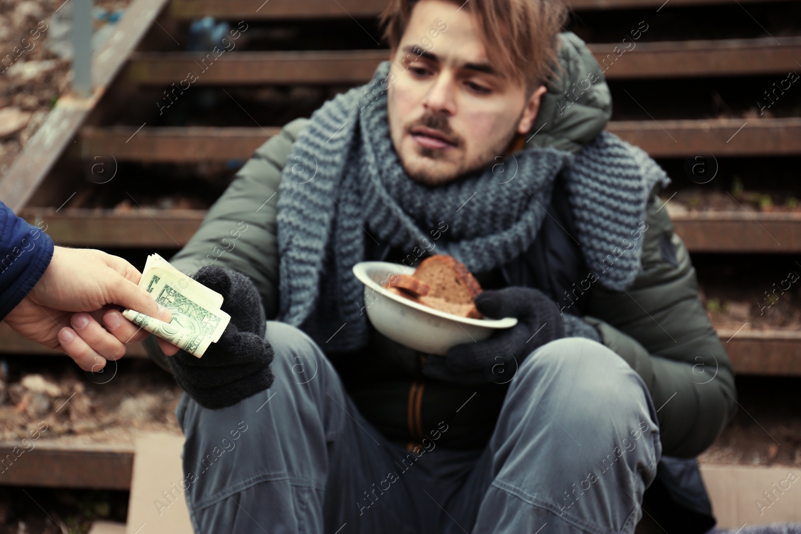 Photo of Poor young man begging for money on stairs outdoors, closeup