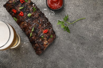 Photo of Glass of beer, tasty grilled ribs and sauce on grey table, flat lay. Space for text