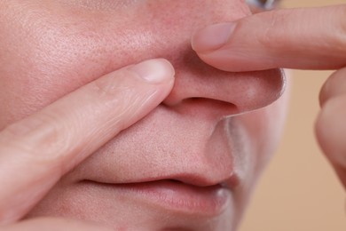 Photo of Woman popping pimple on her nose against beige background, closeup