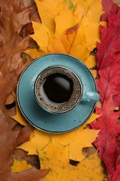 Cup of hot coffee on autumn leaves, top view