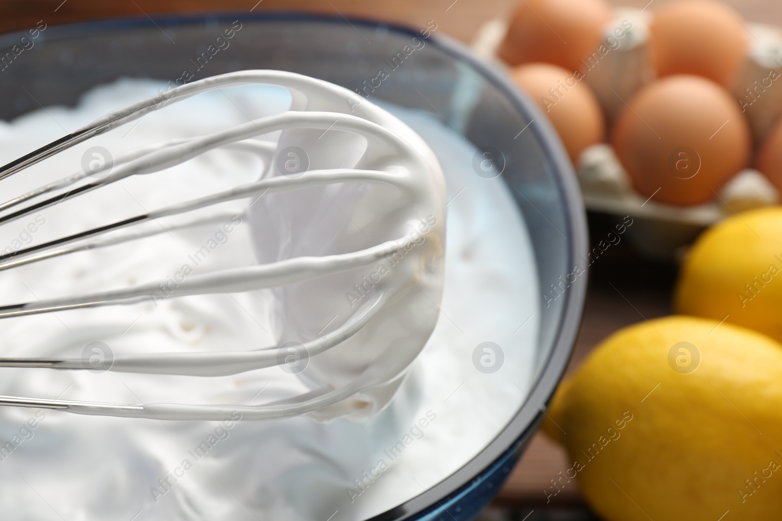 Photo of Bowl with whipped cream, whisk and ingredients on table, closeup
