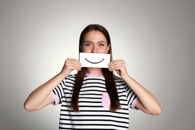 Woman holding sheet of paper with smile on grey background