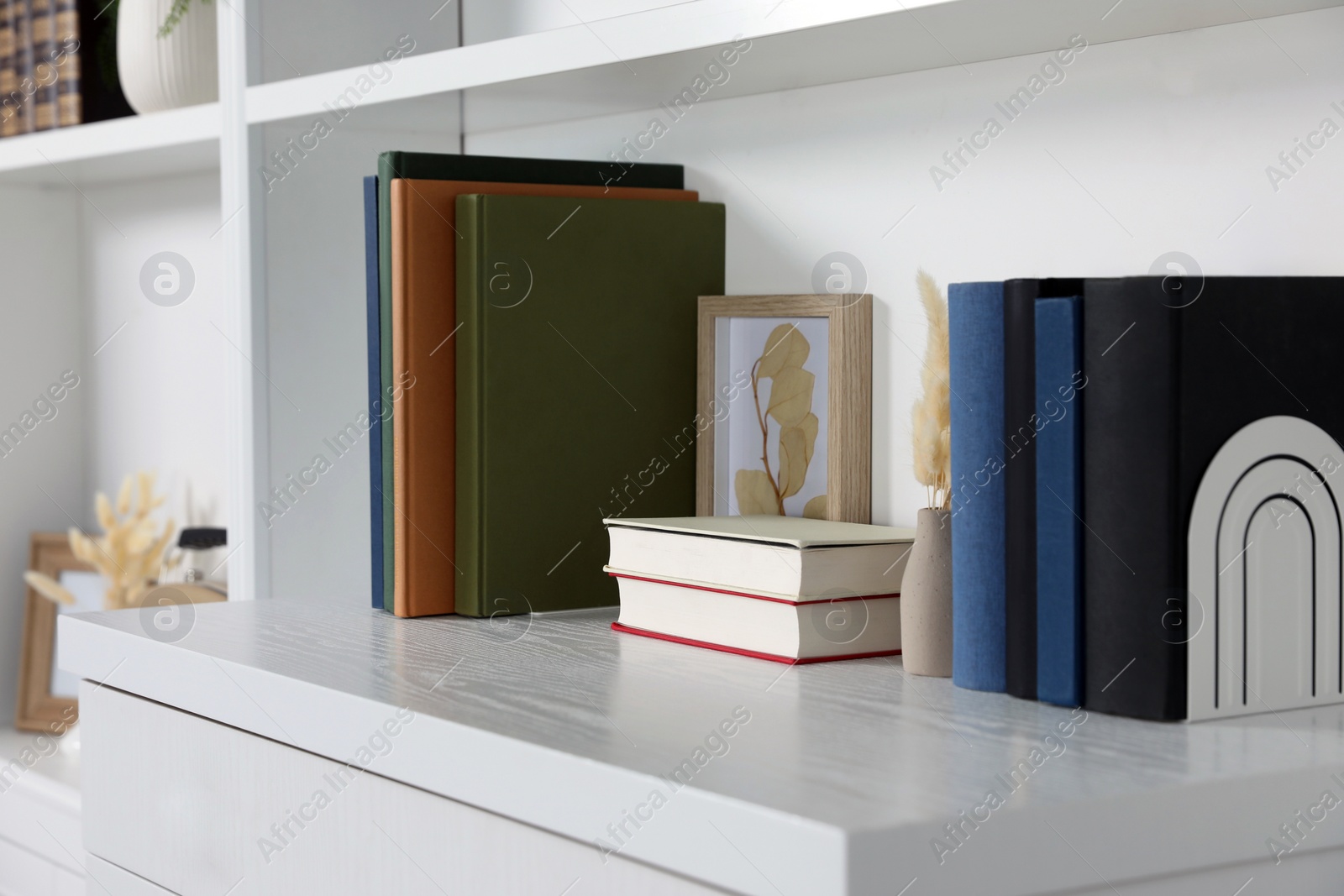 Photo of Hardcover books, picture and vase with dry flowers on shelving unit