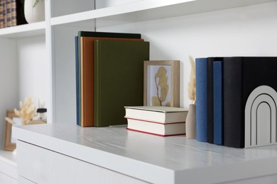 Photo of Hardcover books, picture and vase with dry flowers on shelving unit