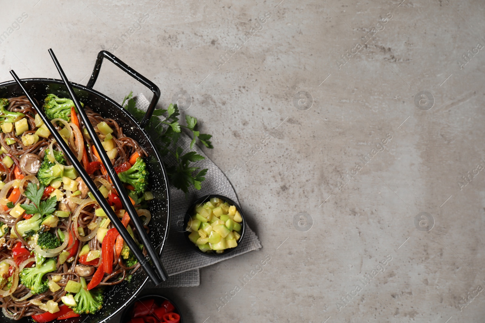 Photo of Stir-fry. Tasty noodles with meat in wok, chopsticks and ingredients on grey textured table, flat lay. Space for text