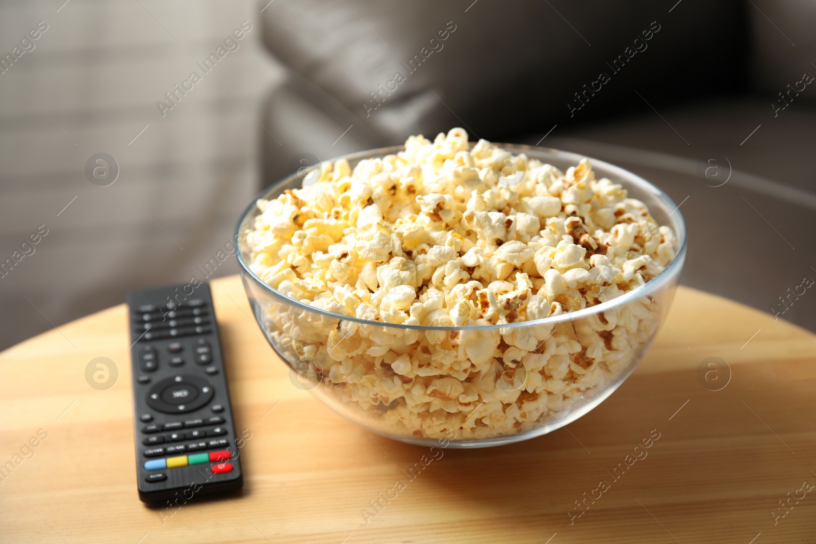 Photo of Bowl of popcorn and TV remote on table against blurred background. Watching cinema