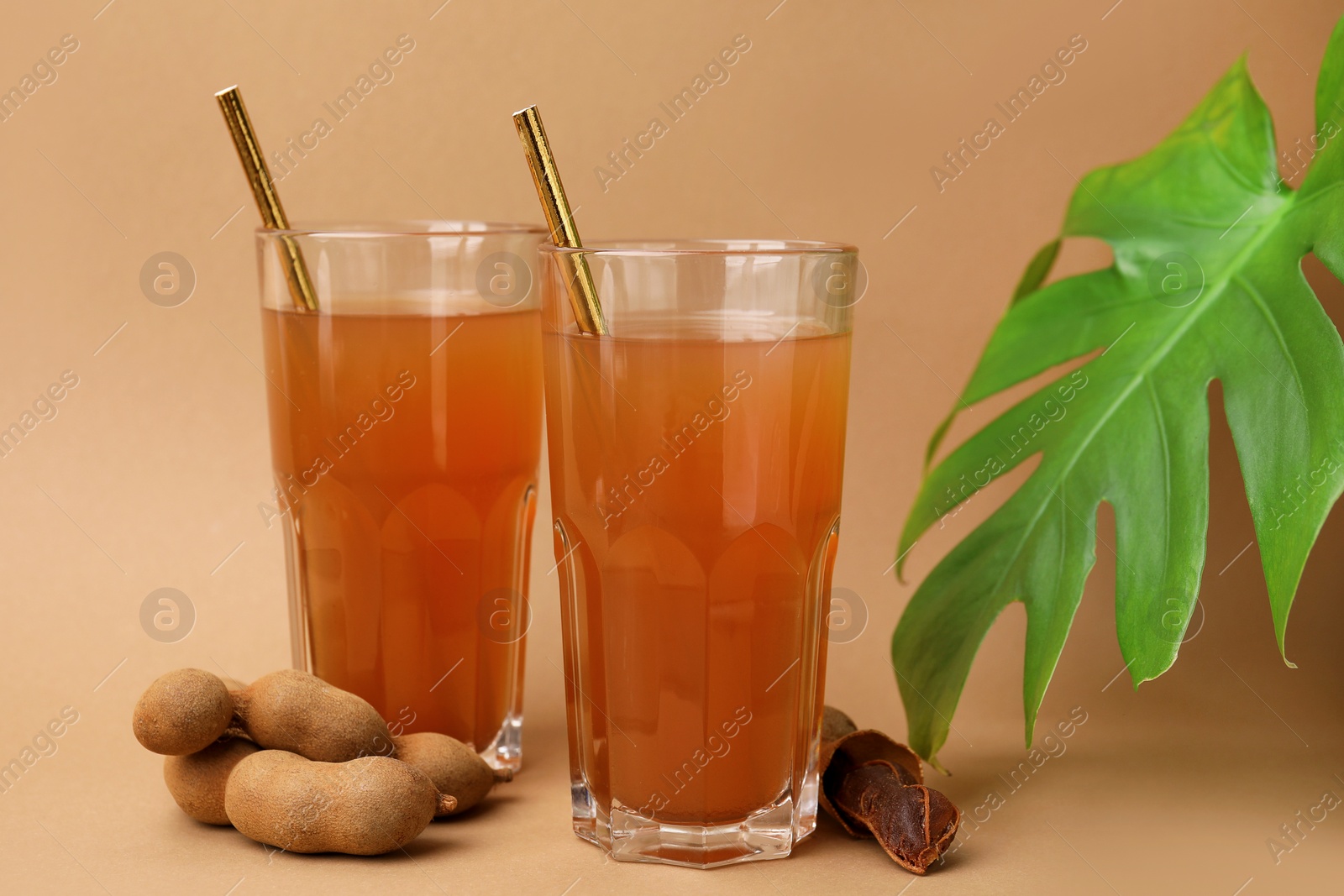 Photo of Tamarind juice, fresh fruits and green leaf on pale brown background