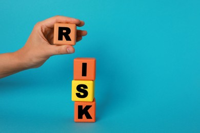 Photo of Woman making word Risk with colorful cubes on turquoise background, closeup. Space for text