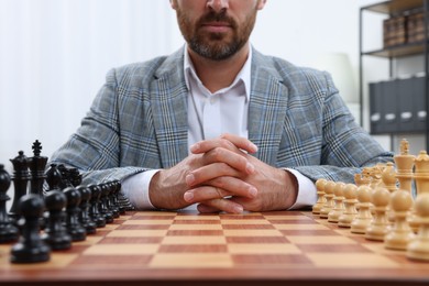 Man with chess pieces on board before game indoors, closeup