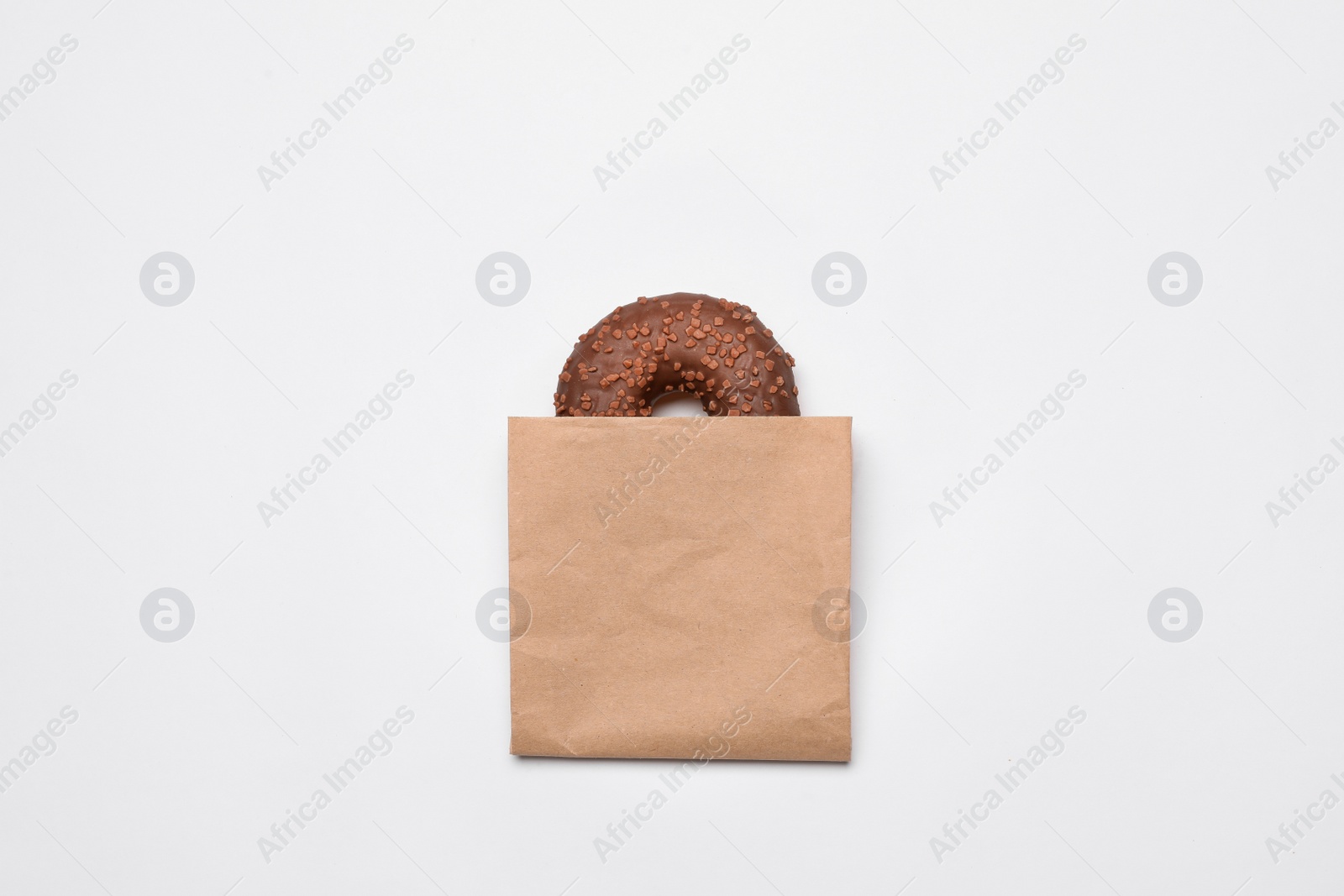 Photo of Paper bag with chocolate doughnut on white background, top view. Space for design