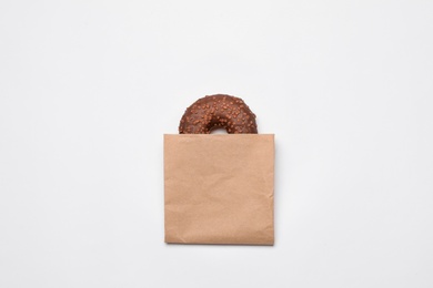 Paper bag with chocolate doughnut on white background, top view. Space for design