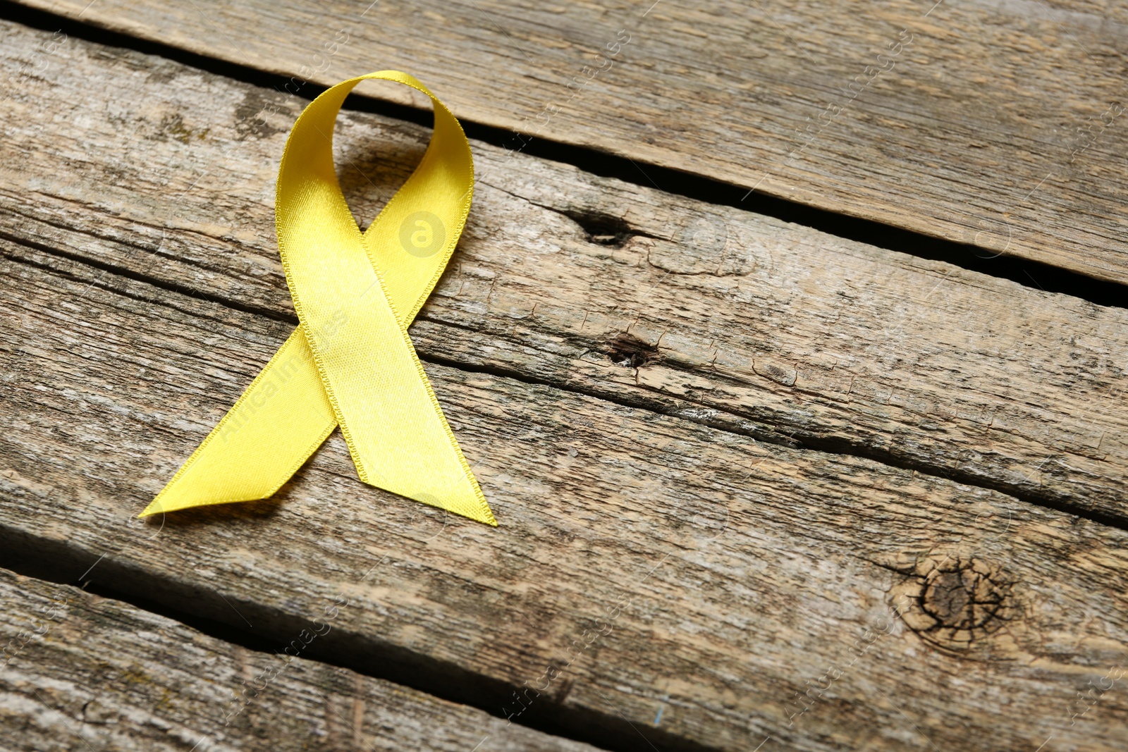 Photo of Yellow awareness ribbon on wooden table, above view. Space for text