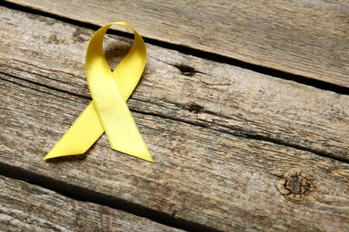 Yellow awareness ribbon on wooden table, above view. Space for text