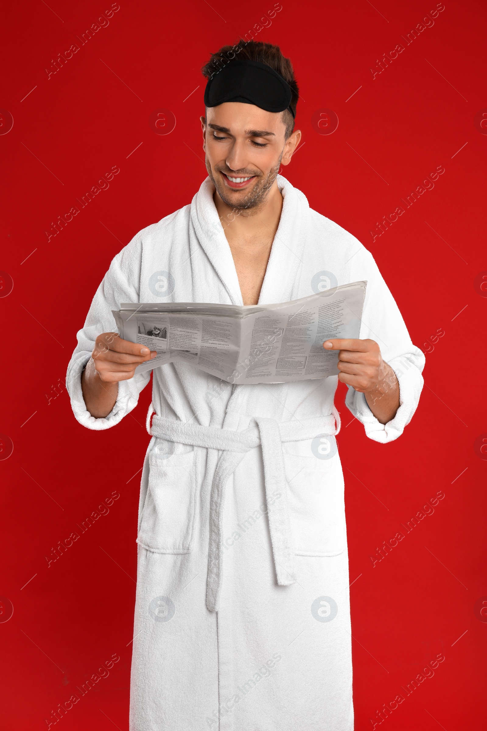 Photo of Happy young man in bathrobe reading newspaper on red background