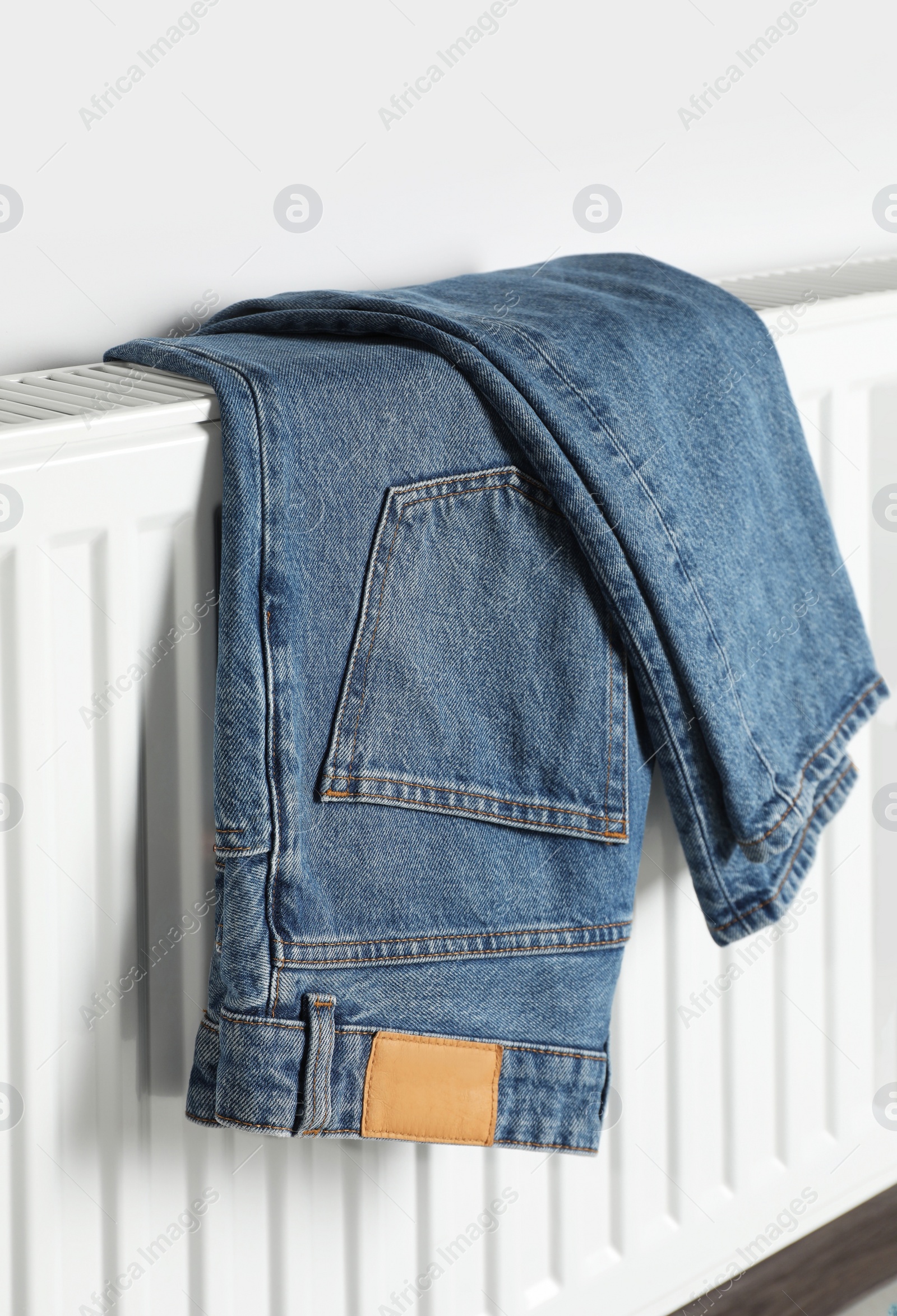 Photo of Blue jeans hanging on white radiator indoors