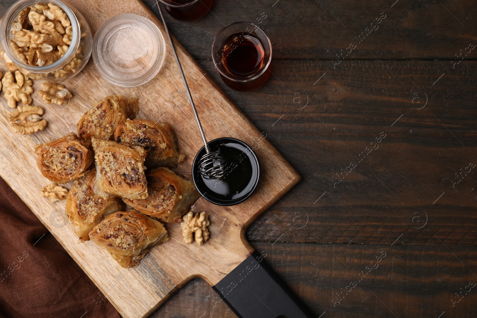 Photo of Eastern sweets. Pieces of tasty baklava, walnuts and tea on wooden table, flat lay. Space for text