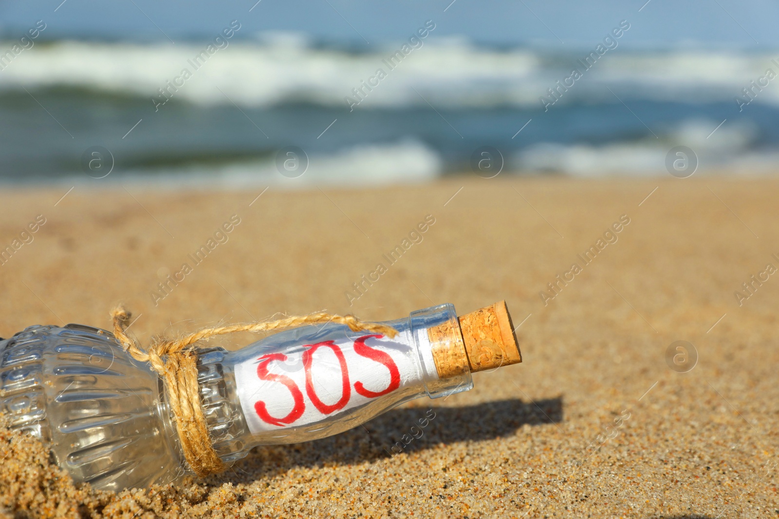 Photo of Glass bottle with SOS message on sand near sea, space for text