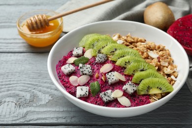 Photo of Bowl of granola with pitahaya, kiwi and almonds on grey wooden table