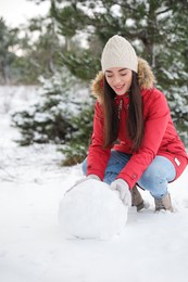 Young woman rolling snowball outdoors on winter day