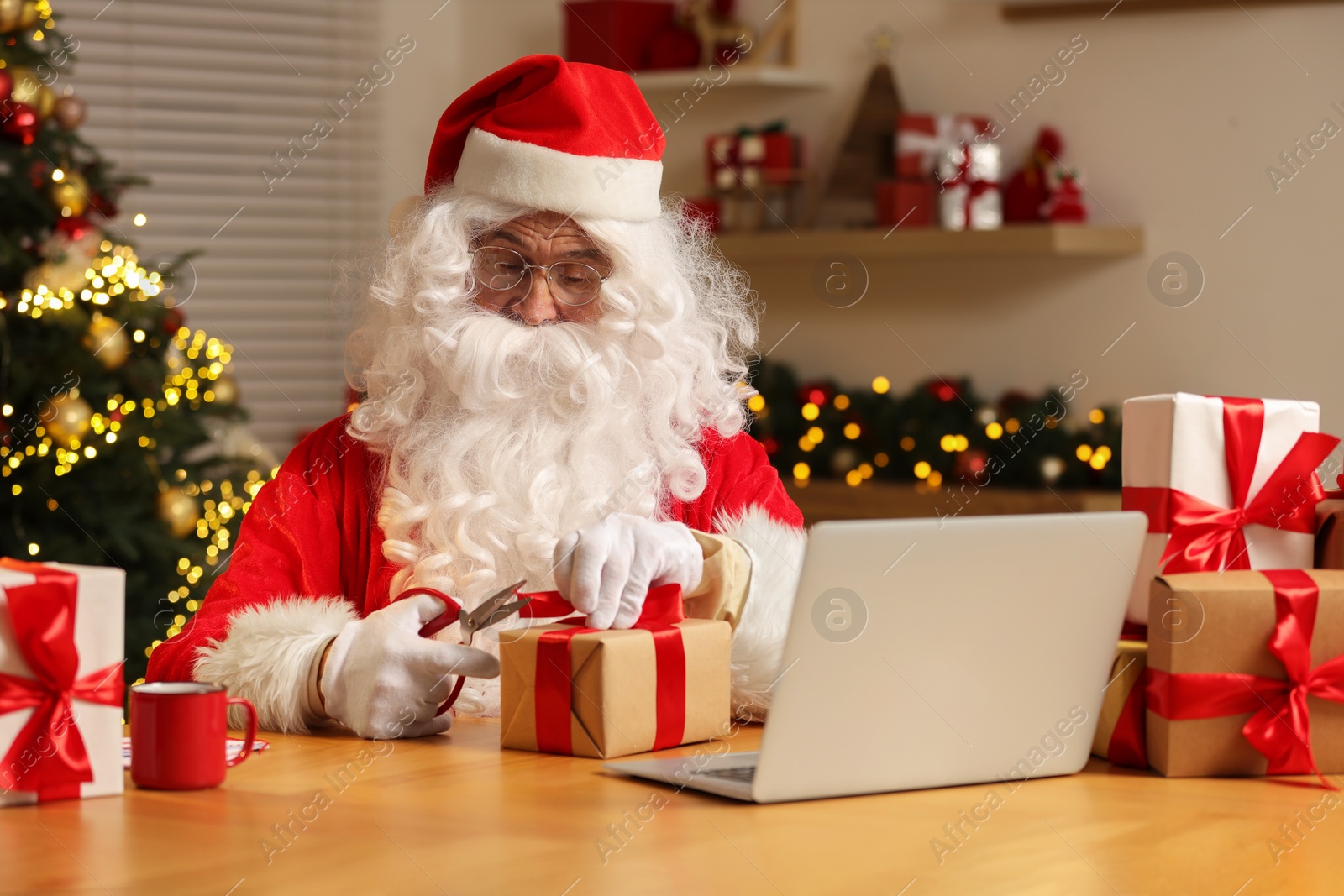 Photo of Santa Claus with scissors decorating Christmas gift at home