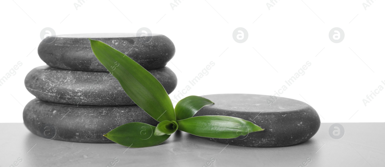 Photo of Black spa stones with bamboo on table against white background. Space for text