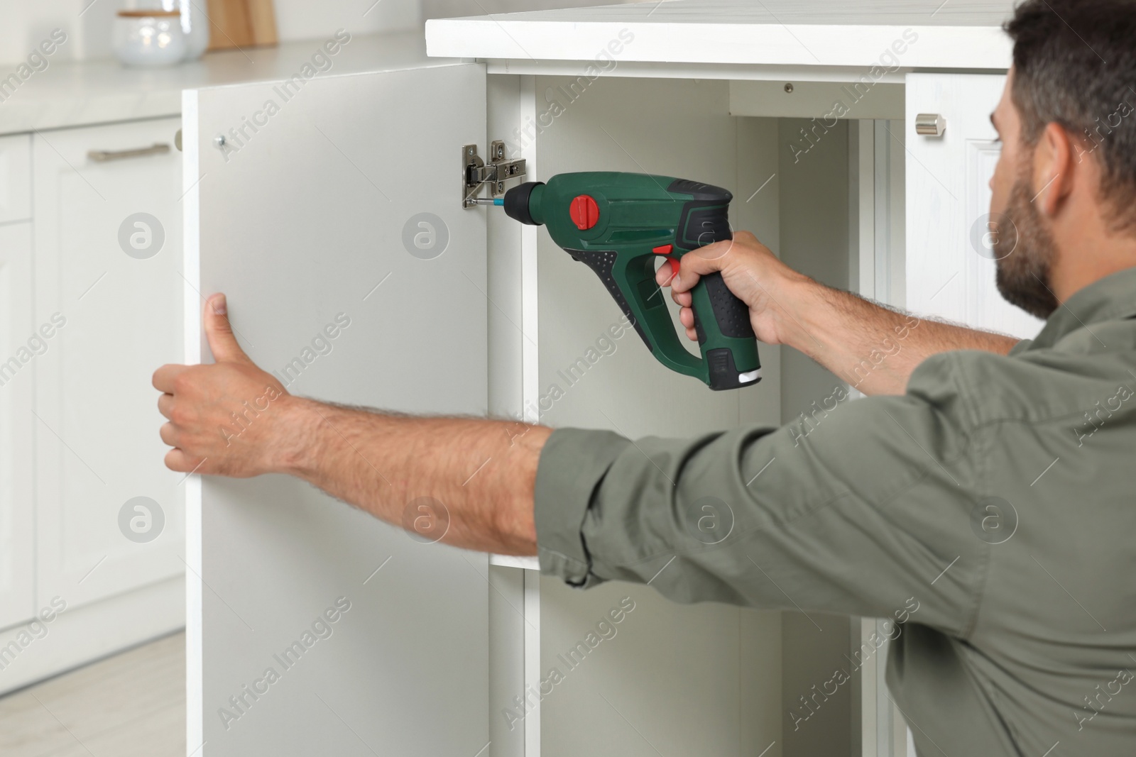 Photo of Man with electric screwdriver assembling furniture indoors, closeup