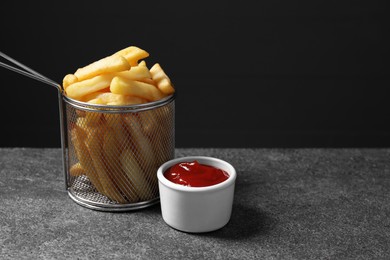 Tasty french fries and ketchup on grey table, space for text
