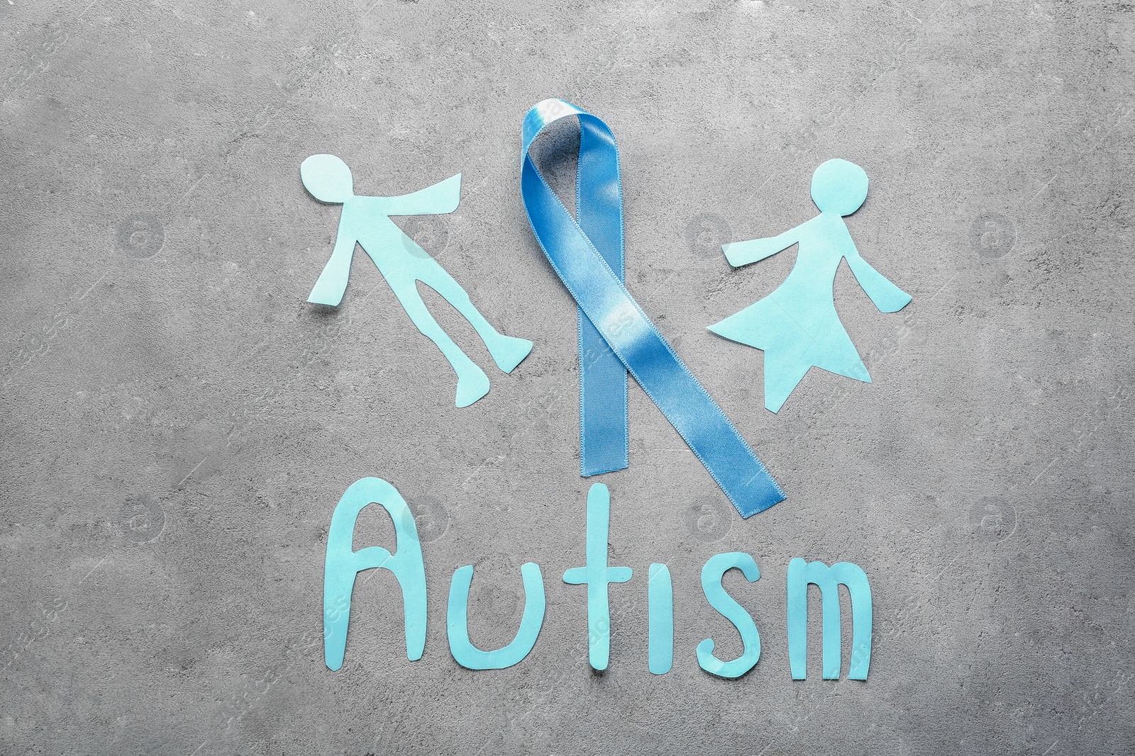 Photo of Word "Autism", paper figures and blue ribbon on light background