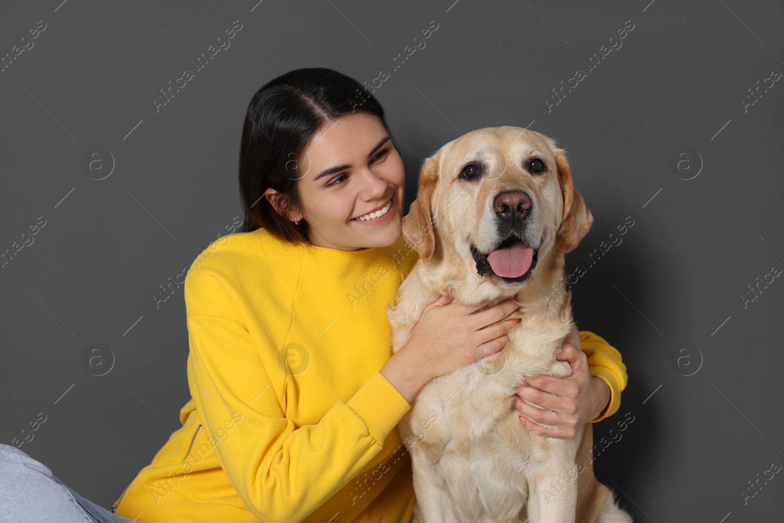 Photo of Happy woman with cute Labrador Retriever against grey wall