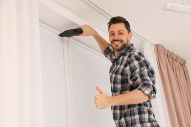 Man with drill installing roller window blind indoors