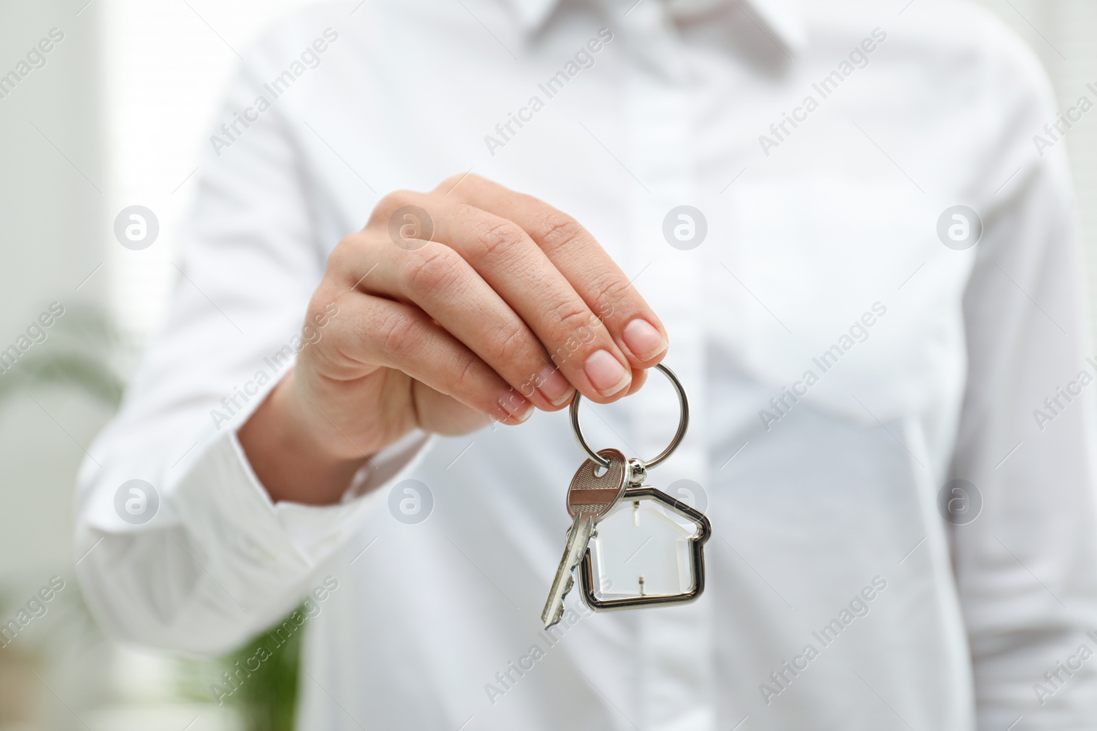 Photo of Real estate agent holding house key with trinket indoors, closeup