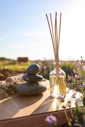 Photo of Composition with reed air freshener on wooden table in blooming lavender field