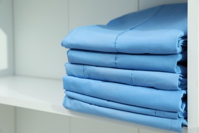 Photo of Light blue medical uniforms on white rack, closeup