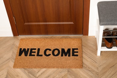 Photo of New clean brown mat with word Welcome near entrance door and shoes shelf