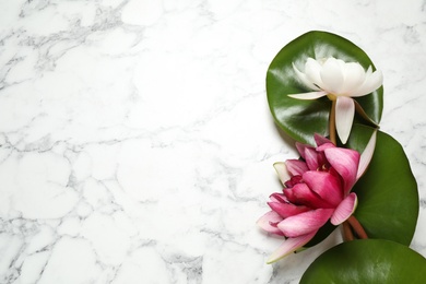 Photo of Beautiful blooming lotus flowers with green leaves on white marble table, flat lay. Space for text