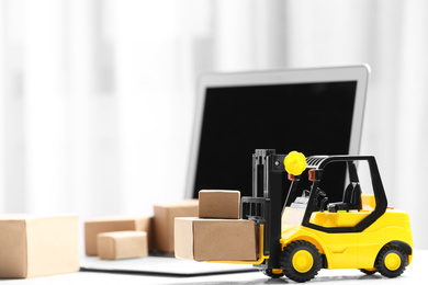 Toy forklift with boxes near laptop on table. Logistics and wholesale concept