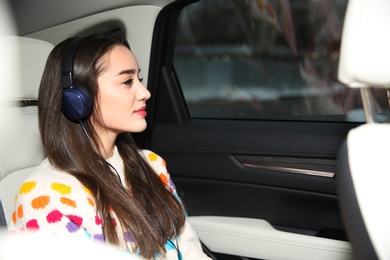 Beautiful young woman listening to music with headphones in car. Space for text
