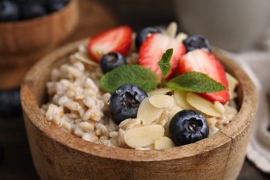 Photo of Tasty oatmeal with strawberries, blueberries and almond petals in bowl on table, closeup