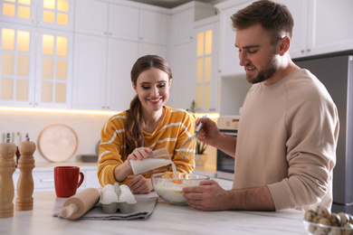 Photo of Lovely young couple cooking dough together in kitchen