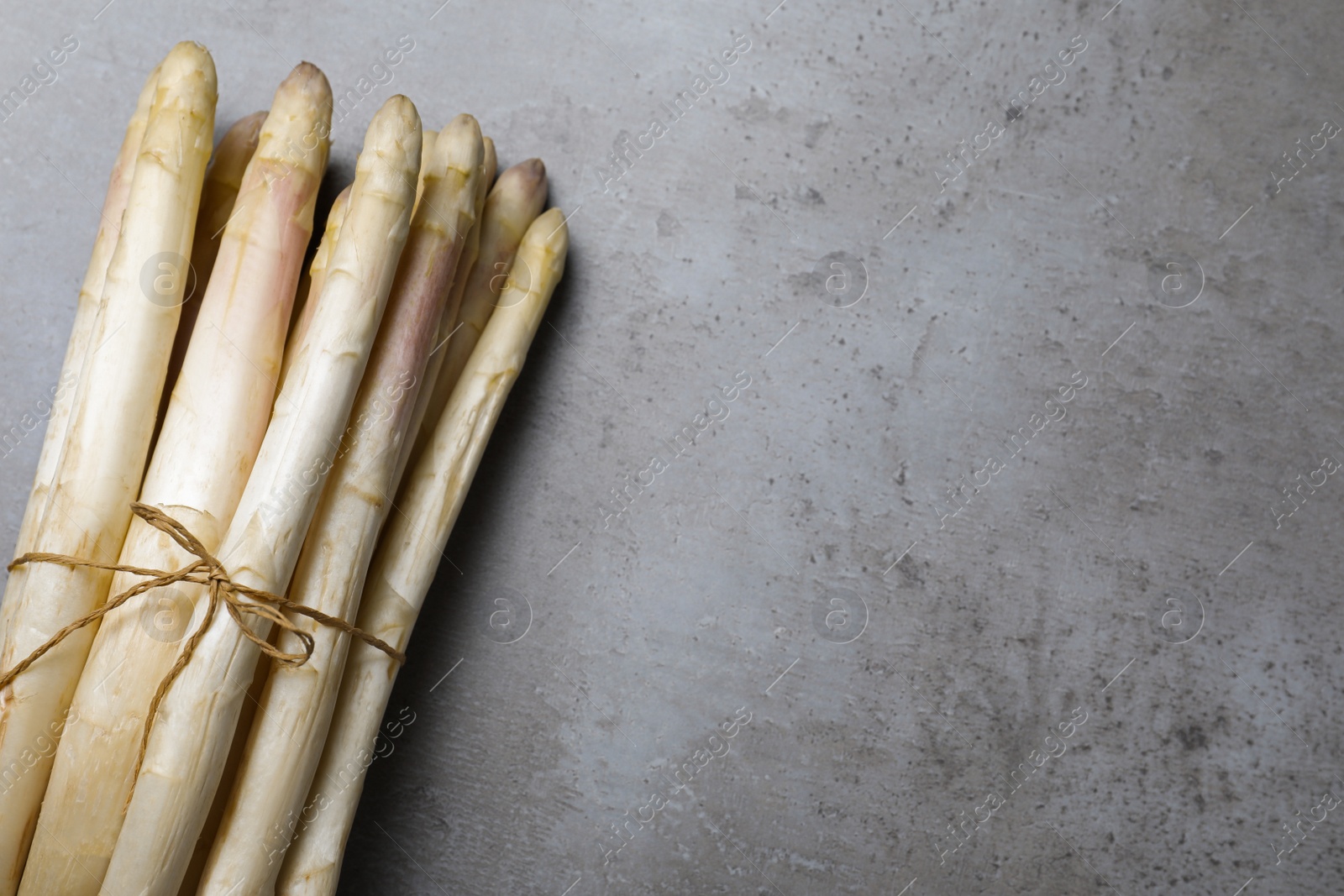 Photo of Bunch of fresh white asparagus on grey table, top view. Space for text