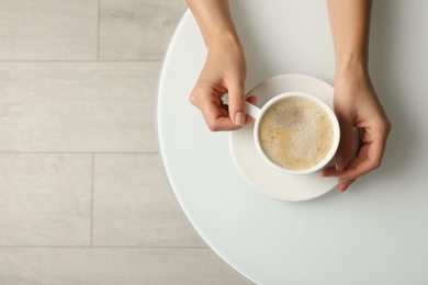 Woman with cup of coffee at white table indoors, top view. Space for text