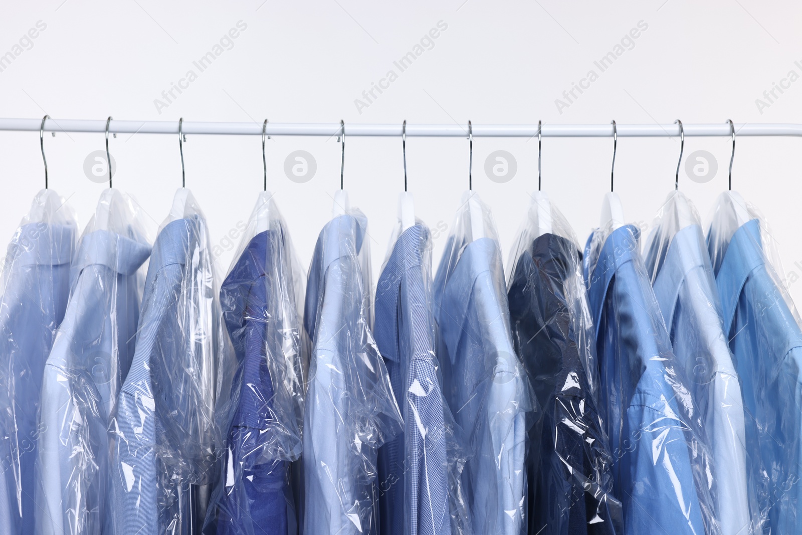 Photo of Dry-cleaning service. Many different clothes in plastic bags hanging on rack against white background, closeup