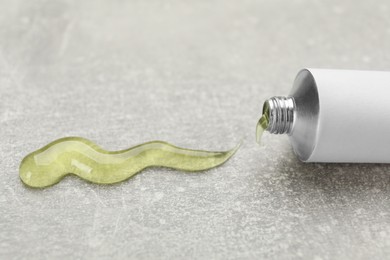 Photo of Open white tube with ointment on light grey table, closeup