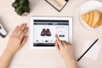 Woman with tablet shopping online at white wooden table, top view