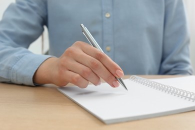 Woman writing with pen in notebook at wooden table, closeup