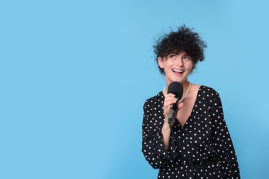 Photo of Beautiful young woman with microphone singing on light blue background. Space for text