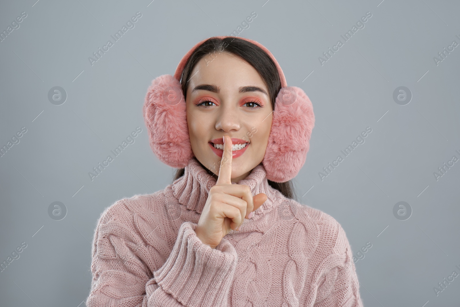 Photo of Beautiful young woman wearing earmuffs on light grey background